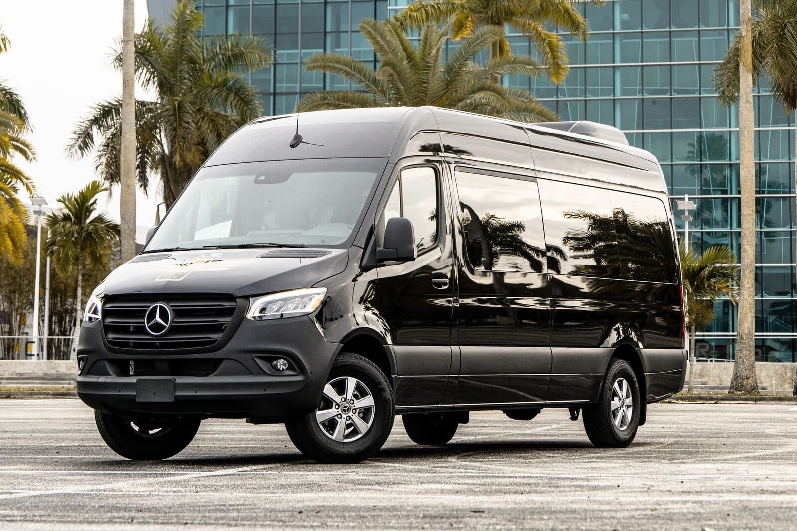Black Mercedes-Benz Sprinter executive van parked outside a modern glass building